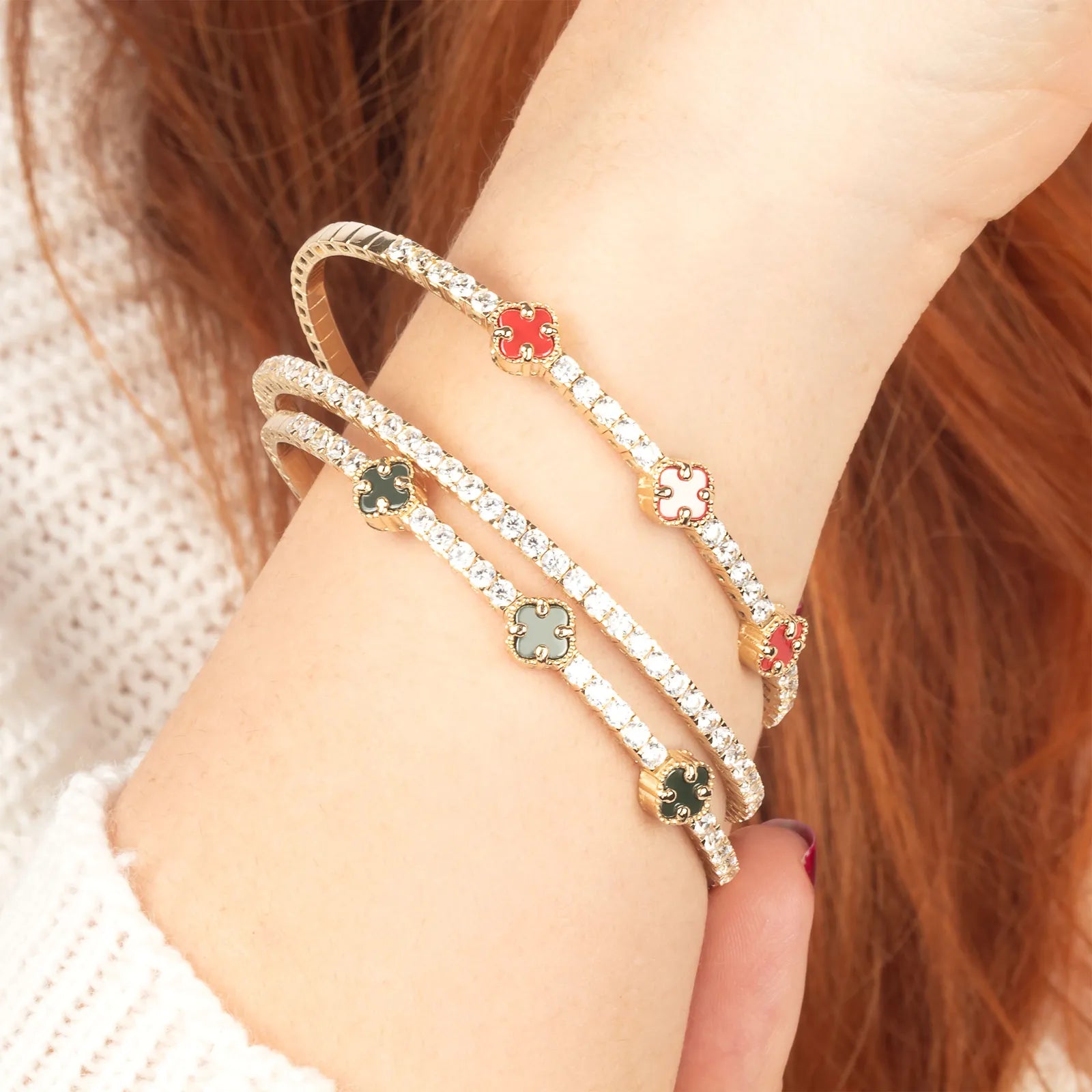 A refined 14K gold tennis bracelet with red and green enamel clover charms and diamond accents, blending classic charm with modern luxury."