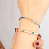 A model wearing an 4K gold bangle with vibrant gemstones, stacked with an emerald clover bracelet for a chic style.