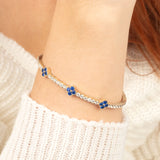A delicate 14K gold bangle bracelet with sparkling moissanite and blue sapphire flower charms, offering a timeless and sophisticated look.