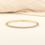 A delicate gold diamond tennis bracelet elegantly displayed on a soft beige fabric, emphasizing its timeless design and premium craftsmanship.
