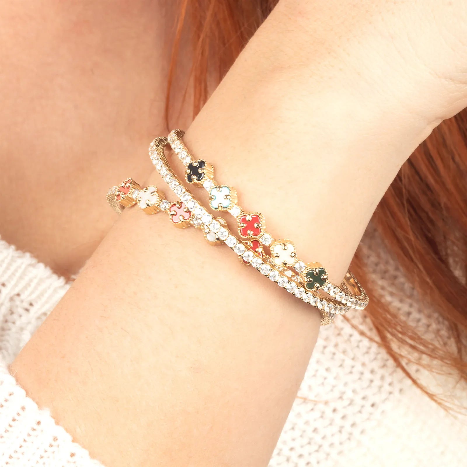 A trendy wrist stack featuring gold tennis bracelets with enamel clover and diamond accents, perfect for layering.