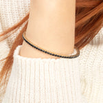 A high-end gold bangle bracelet featuring a row of exquisite black diamonds, designed for an effortlessly chic look.