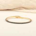 A sophisticated gold tennis bracelet encrusted with black diamonds, offering a classic yet modern touch to any outfit.