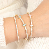 A stylish wrist adorned with layered pastel blue, pink, and white enamel clover diamond tennis bracelets in gold, creating a delicate and fashionable aesthetic.