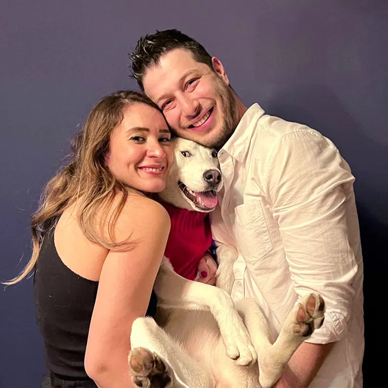 Kaan and Arzu, the founders of MyJewelist, smiling and holding their white Husky. Their passion for meaningful jewelry drives the brand’s vision.