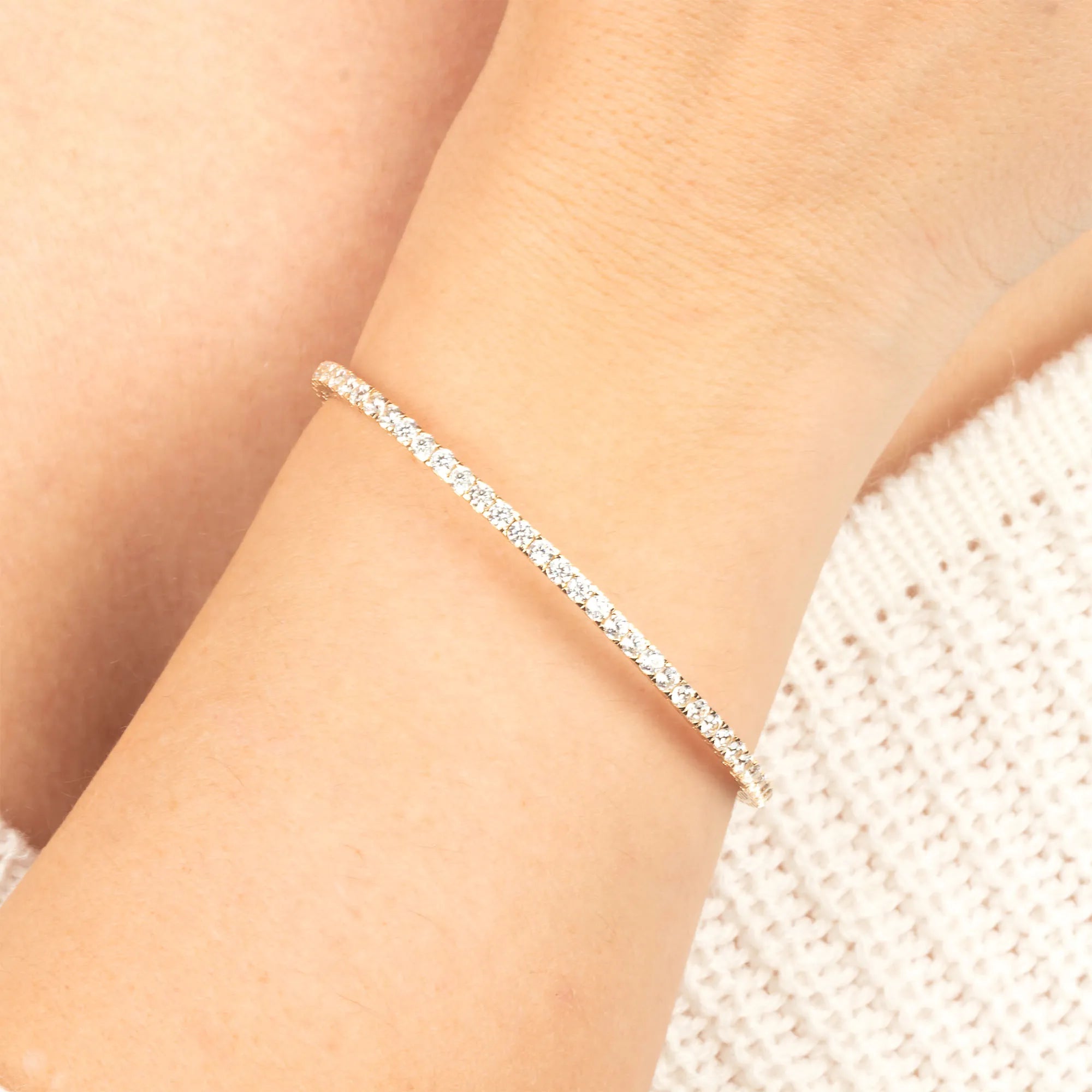 A close-up of a 14K gold diamond tennis bracelet worn on a woman’s wrist, showcasing its sleek, minimalist elegance.