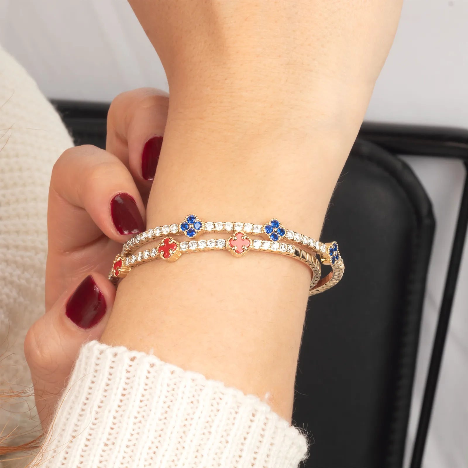 A stylish gold bracelet featuring vibrant red and blue enamel clover charms with sparkling stones, designed for effortless layering and elegance."