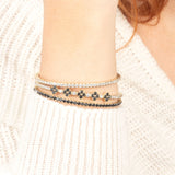 A fashionable wrist stack featuring gold tennis bracelets with sparkling white and black stones, adding a bold and elegant touch.