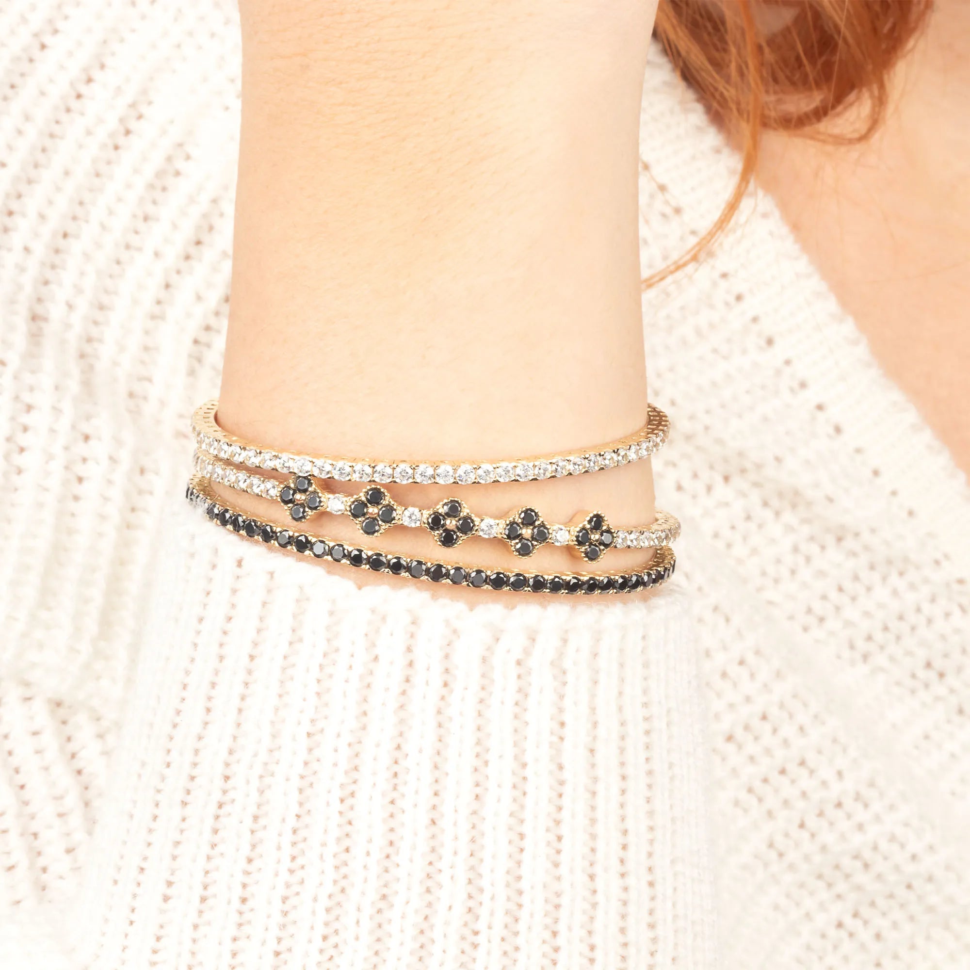 A fashionable wrist stack featuring gold tennis bracelets with sparkling white and black stones, adding a bold and elegant touch.