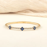 A luxurious and flexible 14K gold bracelet with blue sapphire floral details and shimmering moissanite accents, perfect for gifting.