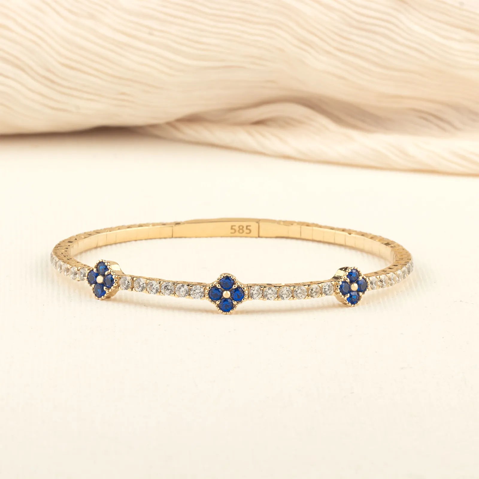 A luxurious and flexible 14K gold bracelet with blue sapphire floral details and shimmering moissanite accents, perfect for gifting.