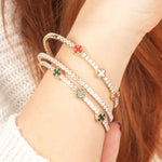 A refined 14K gold tennis bracelet with red and green enamel clover charms and diamond accents, blending classic charm with modern luxury."
