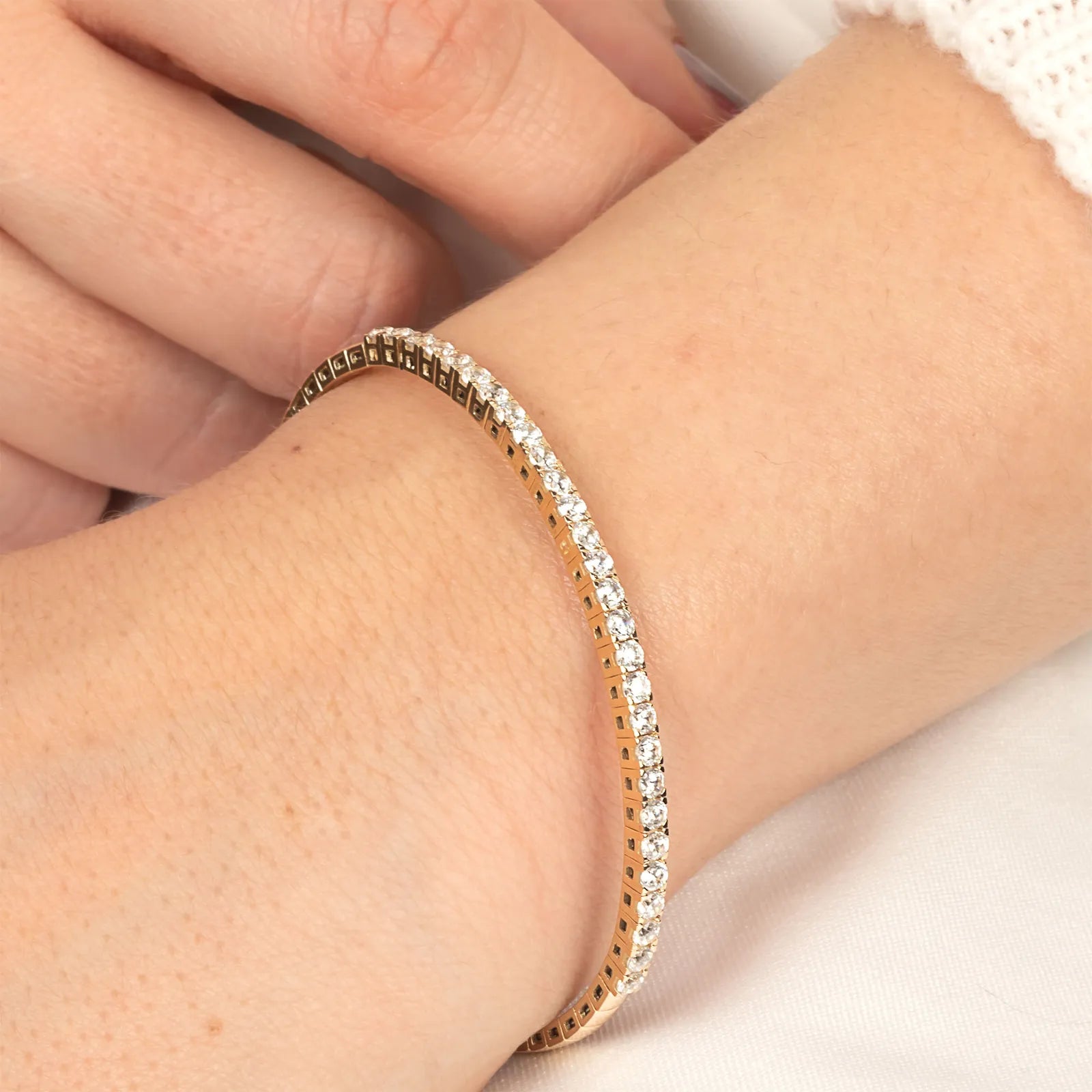 A woman adjusting her gold moissanite tennis bracelet, showcasing its flexible fit and luxurious craftsmanship.