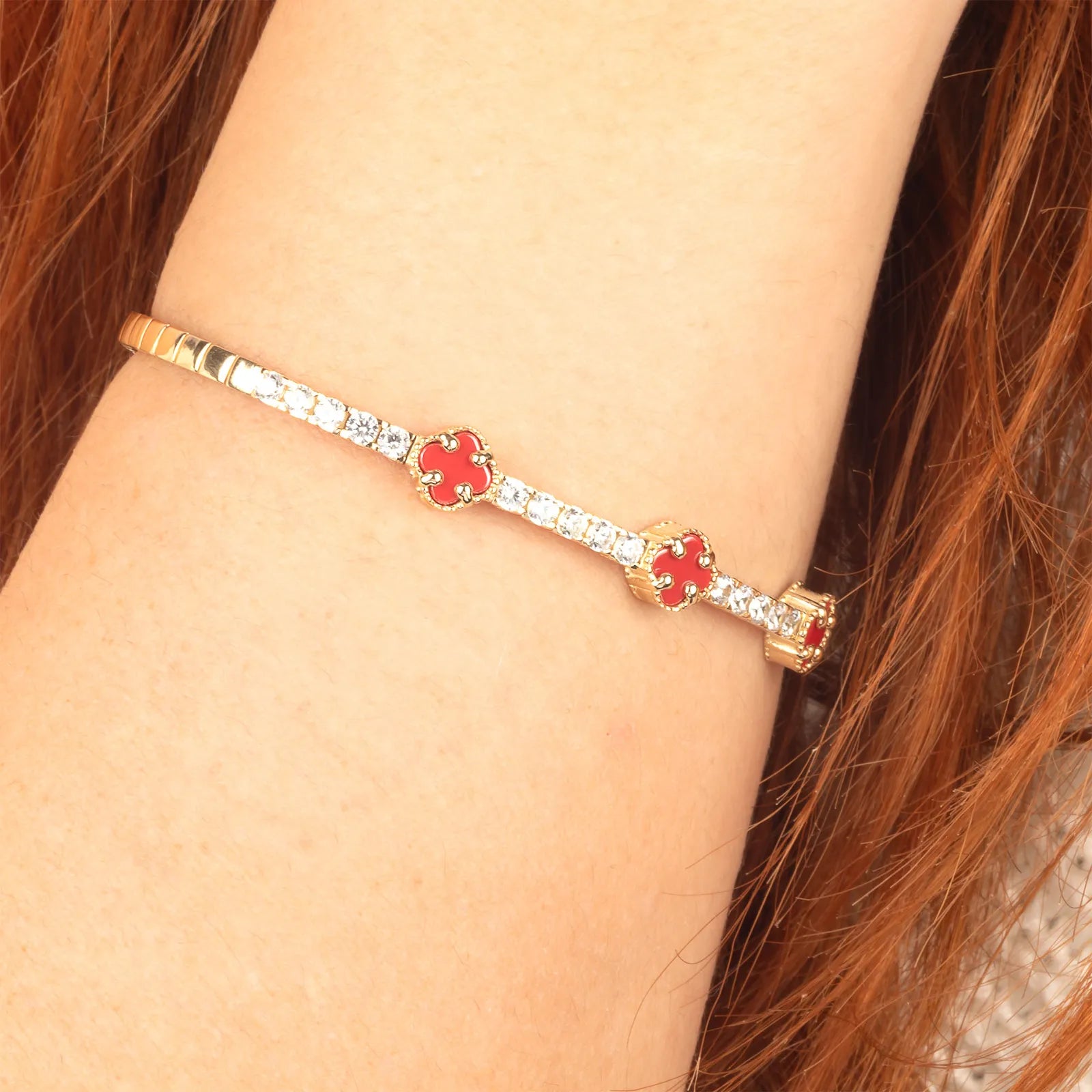 A luxurious gold tennis bracelet with sparkling diamonds and clover-shaped aqeeq charms in red adding a refined touch to any outfit.