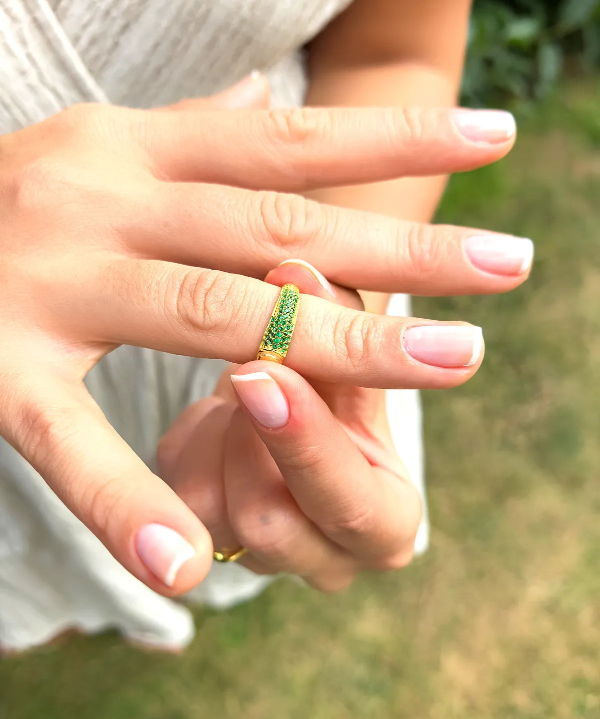 Close-up of a hand wearing a green ring with a blurred natural background