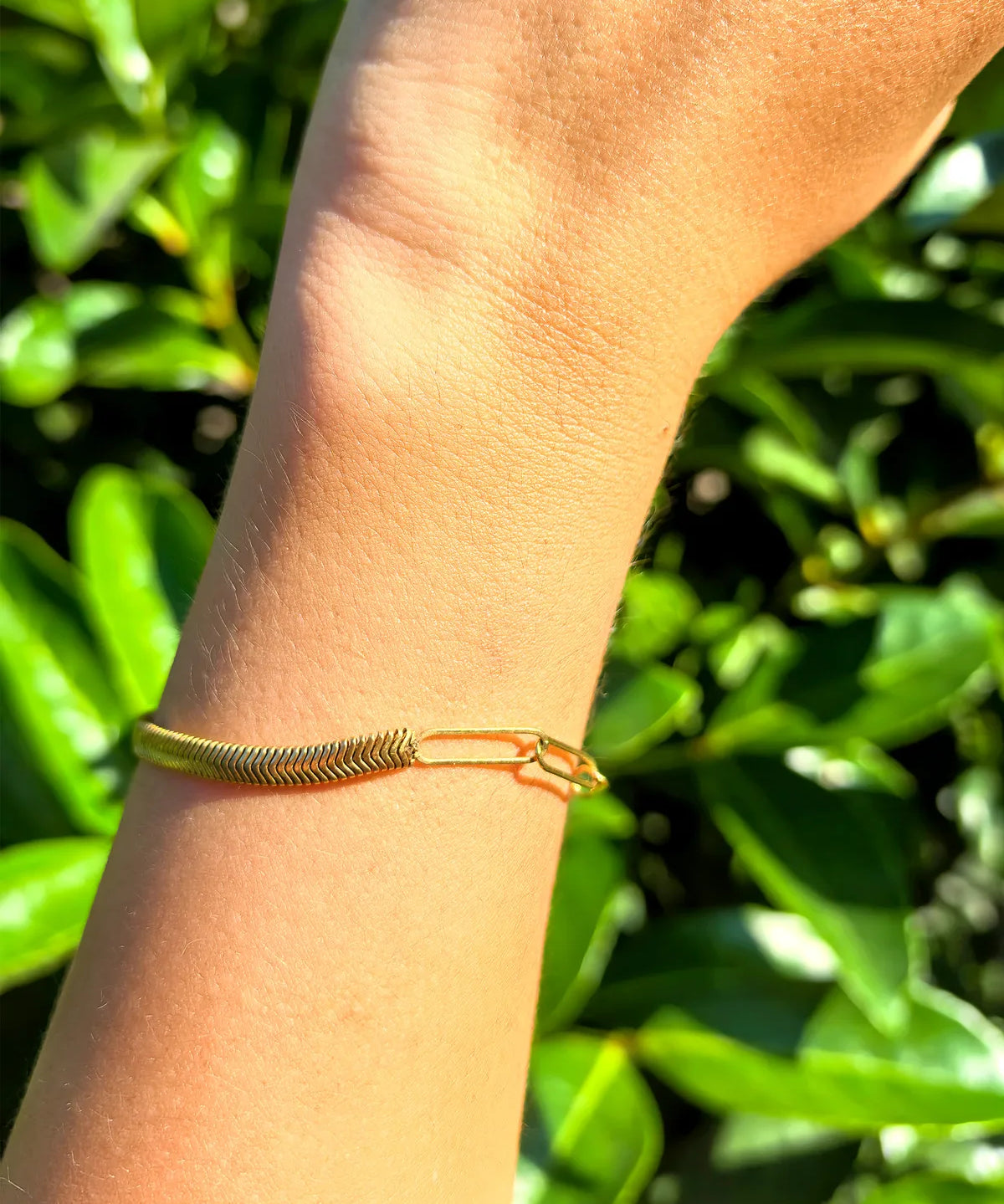 Gold bracelet on a wrist with a green leafy background