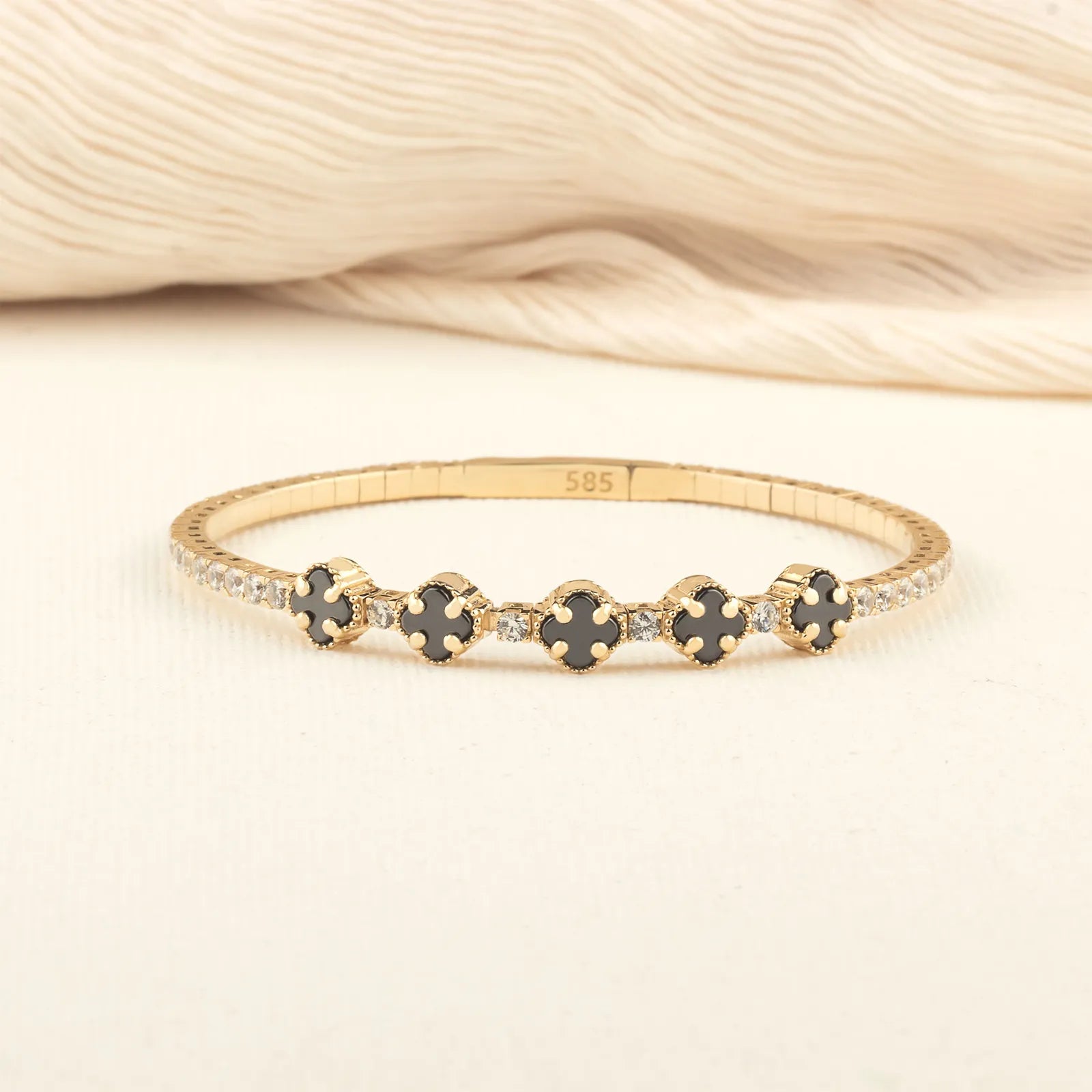 Gold bracelet with black and white gemstones on a neutral background| MyJewelist