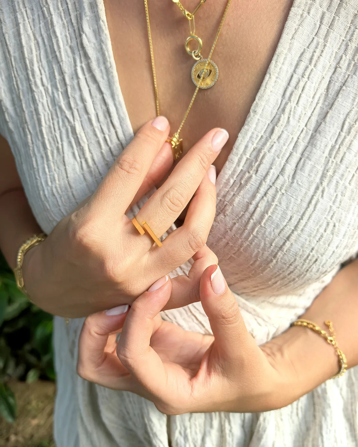 Close-up of hands wearing gold jewelry with a blurred natural background