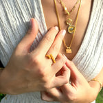Close-up of a person wearing gold necklaces and rings with a blurred natural background
