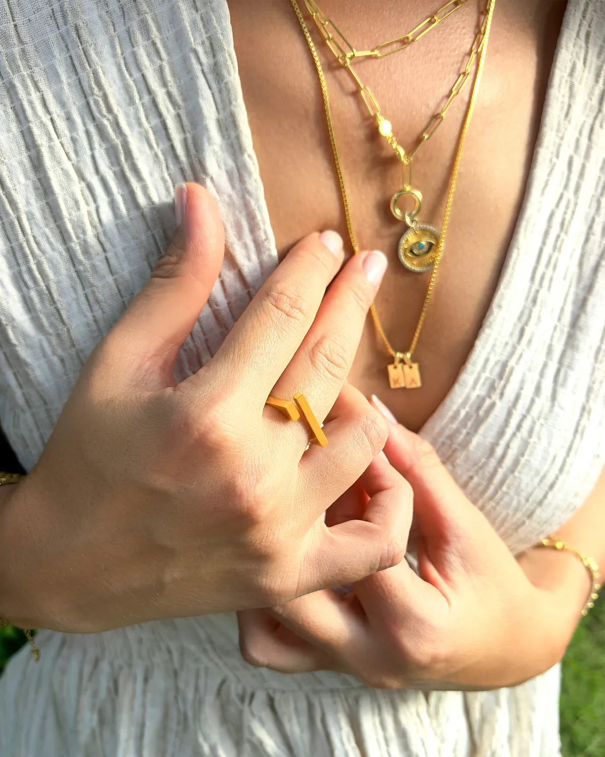 Close-up of a person wearing gold necklaces and rings with a blurred natural background