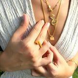 Close-up of a person wearing gold necklaces and rings with a blurred natural background