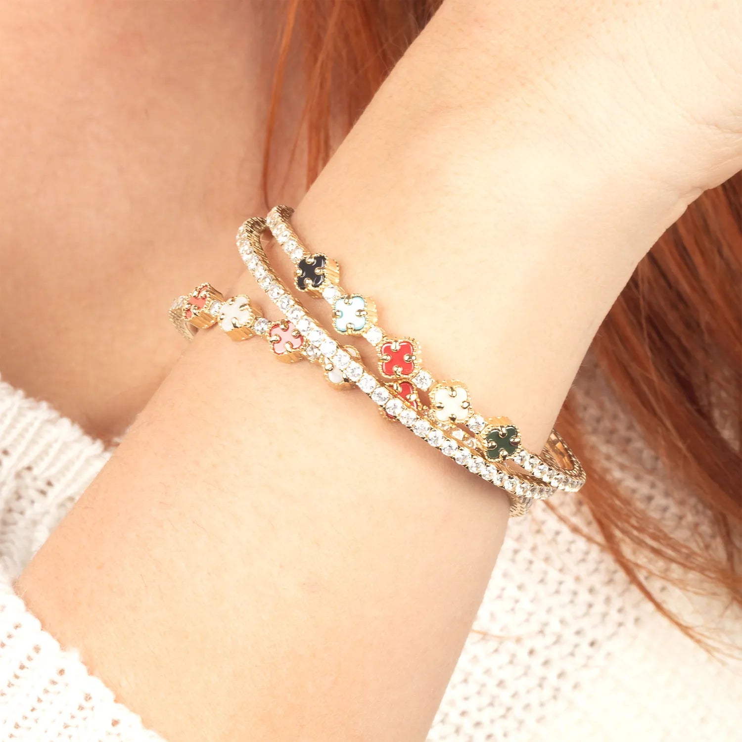 Close-up of a wrist wearing two decorative bracelets with floral and clover charms.
